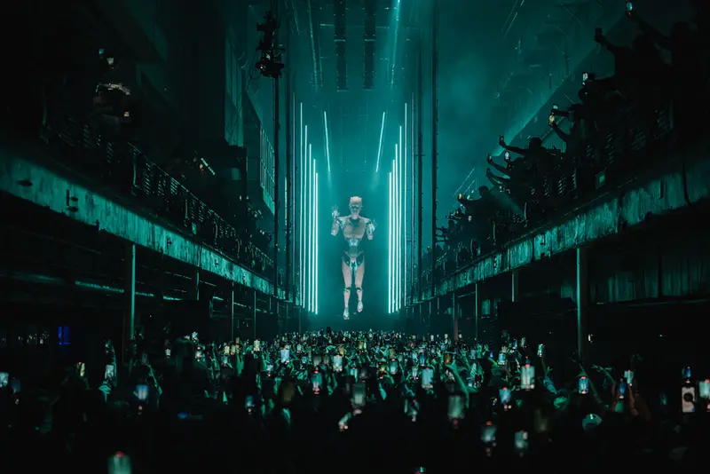 A robotic figure towers over the crowd at an Anyma Afterlife show in teal light