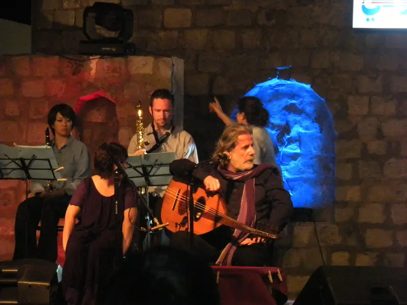 Marcel Khalife performing with musicians in front of a stone wall lit blue