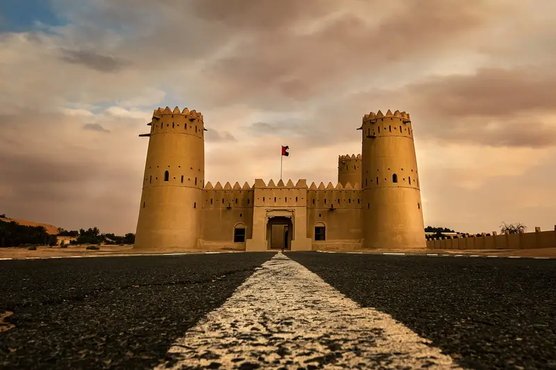 A sandstone fort with twin towers glowing at sunset in the Liwa region